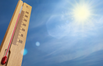 Thermometer showing high temperatures with sun shining in the background